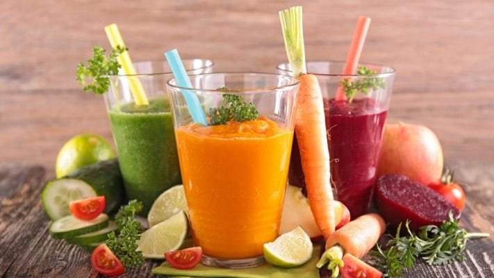 Jugos prensados en frío preparados con un Extractor de Jugo Prensado en Frío KALTER junto a frutas y verduras frescas.